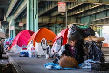 Twitch Napier, who is homeless, sits with her dog, Shiva, near tents set up under the 101 Freeway along Division Street, part of a large homeless encampment, in San Francisco.